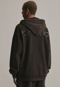 Czarna, oversized bluza z kapturem o miękkiej fakturze, z dużym kapturem i nadrukowanym logo na plecach. Żebrowane mankiety i hem.