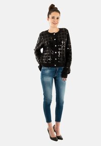 Cardigan noir à sequins avec un motif en grille et des boutons ronds. Associé à un jean ajusté bleu moyen et des escarpins noirs à bouts pointus.