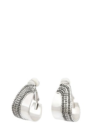 Boucles d'oreilles créoles clipsées ton argent avec motifs noirs texturés à points et lignes sur la surface extérieure, bords arrondis et bandes intérieures lisses.