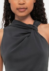 Tumehall sööteta topp drapeeritud kangaga, millel on keerutatud sõlm detailsel õlal, sile tekstuur ja minimalistisch disain.