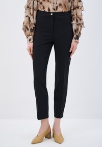 Black fitted trousers with a smooth texture, featuring a front button closure, side seams, and tapered legs, paired with beige heels.