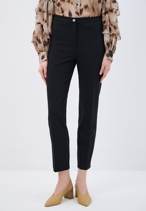 Black fitted trousers with a smooth texture, featuring a front button closure, side seams, and tapered legs, paired with beige heels.