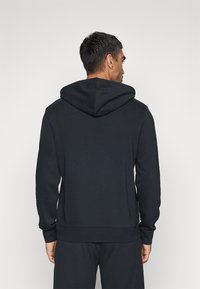 Felpa nera con cappuccio, maniche lunghe e polsini a coste. Presenta un design semplice, realizzata in un tessuto morbido con una texture liscia.