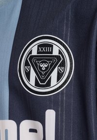 Mörkblå och ljusblå sporttröja med en rund svart logotyp med en triangulär design, ögon och texten "XXIII".