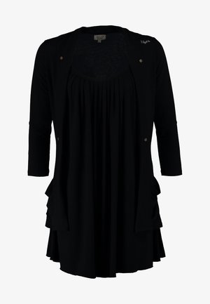 Tunique noire à couches avec des manches courtes, associée à un jean bleu déchiré et des bottines noires à talons. Accessoire : petit sac à main en peau de serpent.