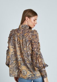 Blusa de estampado de paisley transparente en tonos marrones y amarillos, con un cuello alto y mangas largas con frunces, de silueta holgada.