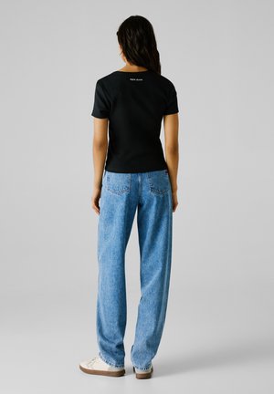 Top nero a maniche corte con texture a coste, abbinato a jeans larghi blu chiaro, con un piccolo logo "Pepe Jeans" sul retro.