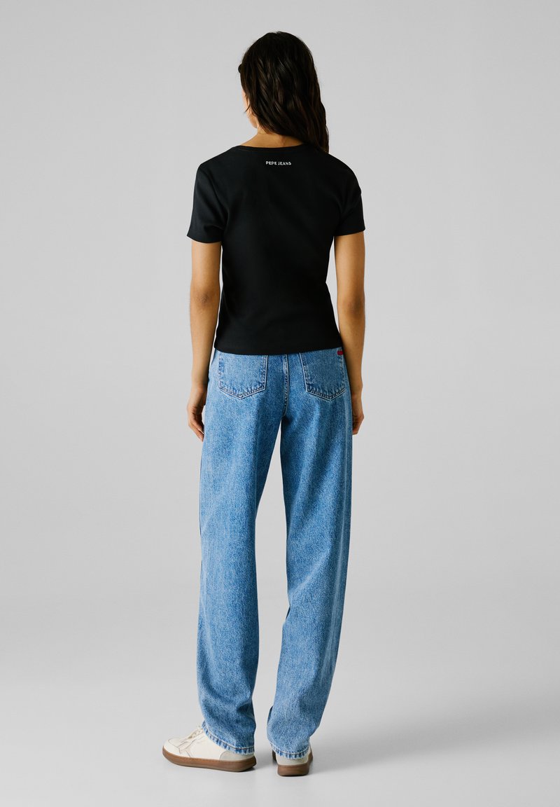 Schwarzes Kurzarm-Top mit gerippter Textur, kombiniert mit hellblauen weiten Jeans, die ein kleines "Pepe Jeans"-Logo auf der Rückseite tragen.