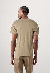 Khaki bomulds t-shirt med korte ærmer, crew neck og en glat tekstur, båret med lysebeige bukser, vist fra ryggen.