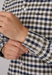 Chemise pour homme à boutons avec un motif à carreaux bleu marine, olive et blanc. En matières en coton avec un col classique et des poignets à un bouton.