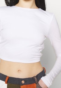 Weißes, kurzes Langarmtop aus elastischem Material mit schlichtem Rundhalsausschnitt und glatter Textur.