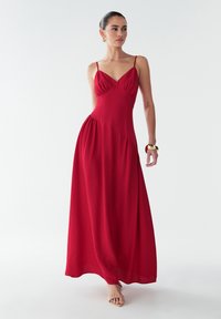 Vestido maxi rojo con tirantes finos, escote en V, detalles fruncidos en el busto y en los laterales, y una tela fluida que cae hasta los tobillos.