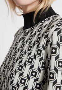 Maglione con un motivo geometrico in bianco e nero, caratterizzato da esagoni e rombi; colletto alto nero; tessuto testurizzato.