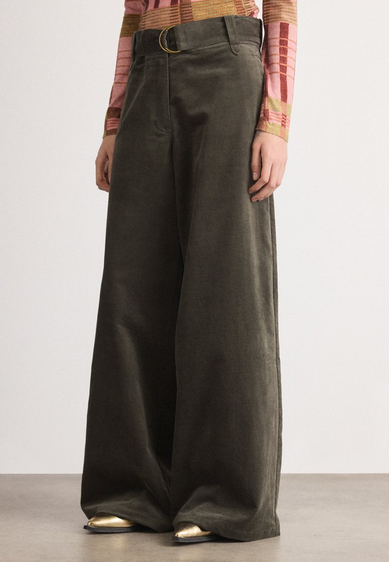 Pantalons larges en velours côtelé vert olive, avec une taille haute, des passants de ceinture et une grande boucle de ceinture ronde. Texture lisse et coupe ajustée.