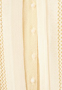Cardigan en maille crème avec des motifs alternés en maille unie et en dentelle, et une rangée de boutons nacrés au centre.
