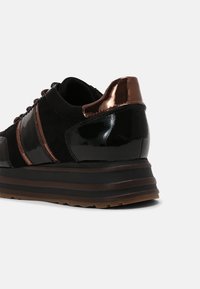 Baskets noires avec des accents métalliques noirs brillants et bronze, semelle plateforme rayée, vues de côté arrière sur fond blanc.