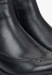 Czarne skórzane botki za kostkę z okrągłym noskiem, detalami w stylu brogue i teksturowanym wykończeniem. Gładkie boki z elastycznymi panelami ułatwiającymi zakładanie.