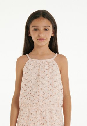 Lace top in soft pink, featuring floral cutout patterns, thin straps, and a gathered neckline, paired with an elastic waist for a relaxed fit.