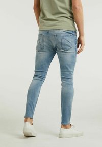 Ljusblå slim-fit jeans med en klassisk femficksdesign, som har blekta detaljer och en jämn textur, tillsammans med vita sneakers.