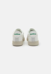 Sneaker bianchi con logo "Reebok" verde, superiore in pelle liscia, colletto imbottito e suola in gomma testurizzata bianco sporco. Design classico a taglio basso.