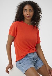 Světlé oranžové tričko s krátkým rukávem vyrobené z měkké tkaniny, doplněné světle modrými džíny s ohrnutými lemy. Jednoduchý design, bez vzorů.