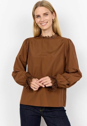 Brown blouse with a high, textured lace collar and puff sleeves. Lace trim at the cuffs adds detail. Paired with dark blue jeans.