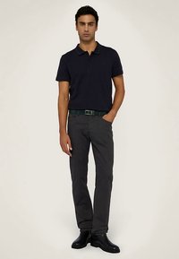 Námořnická polokošile s límečkem, šedé kalhoty a černé kotníkové boty. Model stojí s jednou rukou v kapse a představuje neformální vzhled.