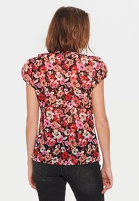 Blouse à imprimé floral avec un fond noir orné de fleurs roses, rouges et crème, manches courtes bouffantes et ourlet arrondi.