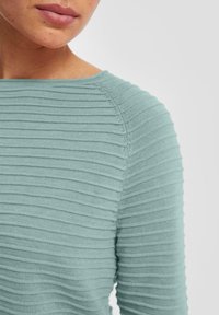 Pull en tricot côtelé turquoise clair avec un col bateau. Présente une texture horizontale et une silhouette ajustée, mettant en avant la douceur et l'élasticité.