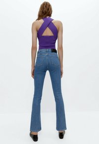 Lila ärmlös topp med korsettdesign på ryggen, tillsammans med ljusblå utsvängda jeans. Svarta skor kompletterar outfiten.