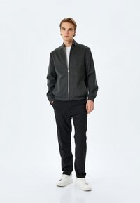 Grå zip-up bomberjakke med ribbede manchetter og kant, parret med sorte pencil-stribede bukser og hvide sneakers. Enkel, moderne design.