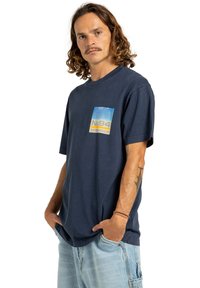 Námořnická modrá bavlněná tričko s krátkým rukávem a kulatým výstřihem. Na levé části hrudi se nachází barevný grafický potisk. Uvolněný střih.