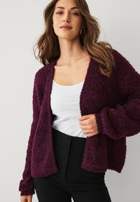 Diep paarse, zachte cardigan met een open voorkant, lange mouwen en geribbelde manchetten, gedragen over een wit shirt, met een losse pasvorm.