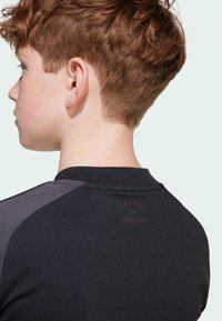 Schwarz-graues Sportoberteil mit kurzen Ärmeln, runder Ausschnitt und erhabenem Text "FREEDOM TO DREAM" auf dem Rücken. Glatte Textur.