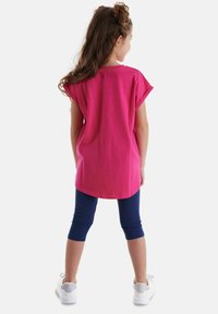Lys pink bomulds t-shirt med korte ærmer, parret med navy capri leggings og hvide sneakers med sølvdetaljer, set fra bag.