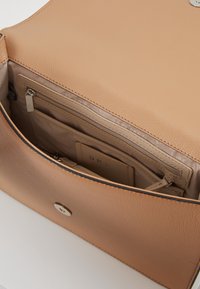 Skórzana torba w kolorze brązowym o chropowatej fakturze, z zamykaną na zamek kieszenią i wnętrzem z przegródkami, zabezpieczona okrągłym metalowym guzikiem.