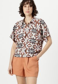Short-sleeve button-up shirt with a floral pattern in coral, navy, and white, paired with light orange shorts. Smooth fabric and relaxed fit.