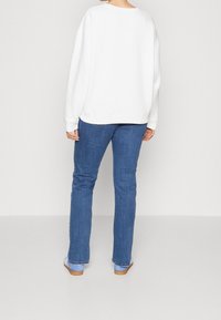 Sudadera blanca de gran tamaño con cuello redondo, combinada con jeans rectos azules. La textura parece suave con puños acanalados.