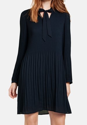 Marinblå plisserad klänning med långa ärmar, v-ringning och knytning vid kragen. Lätt material med en flödande silhuett.