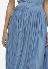 Svetlomodrá plisovaná sukňa s textúrovanou látkou, mäkkým pásom a vertikálnymi záhybmi, ktoré vytvárajú plynulý siluetu.