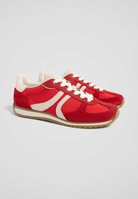 Chaussures de sport rouges présentant un mélange de textures lisses et en suède, des accents blancs, et une semelle en caoutchouc avec une prise texturée.