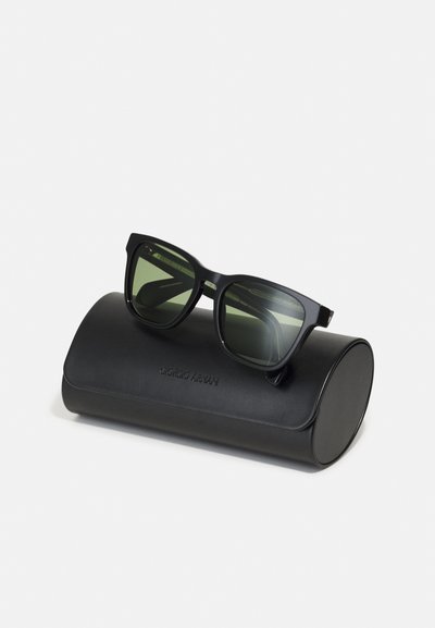 Ochelari de soare dreptunghiulari negri cu lentile verzi, așezați pe un etui oval negru cu text în relief. Etuiul are o textură de piele netedă.