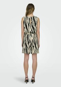 Mouwloze playsuit in beige met abstracte zwarte strepen, voorzien van een keyhole rug, een ceintuur in de taille en shorts, gecombineerd met zwarte hakken.