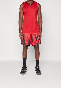 Débardeur de sport rouge avec des accents noirs, associé à un short rouge à motifs géométriques noirs audacieux. Baskets noires avec des touches de vert.