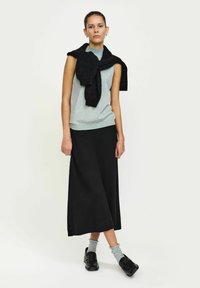 Top gri fără mâneci, fustă lungă neagră, pulover negru aruncat pe umeri, șosete gri și pantofi slip-on negri. Design minimalist.