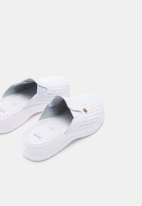 Vita slip-on skor gjorda av perforerat material, med en subtil gyllene accent och en tjock vit sula för extra höjd.