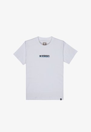 Biała bawełniana koszulka z logo "DC Shoes", niebieskie dżinsy i szare trampki. Dziecko stoi na neutralnym tle, ma krótkie kręcone włosy.