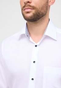 Wit overhemd met patroon op de kraag, blauwe knopen en borstzak. Gladde textuur en reguliere pasvorm, geschikt voor formele gelegenheden.