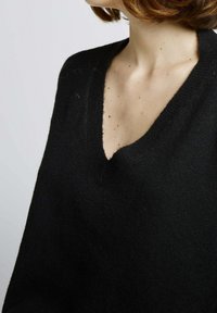 Pull noir à col en V en tissu tricot doux, avec une coupe décontractée et des bords côtelés, visible de l'épaule vers le bas.