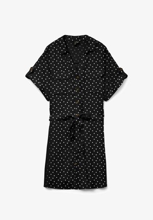 Robe noire à manches courtes boutonnée avec des pois blancs, ceinture nouée à la taille et deux poches poitrine à rabats.